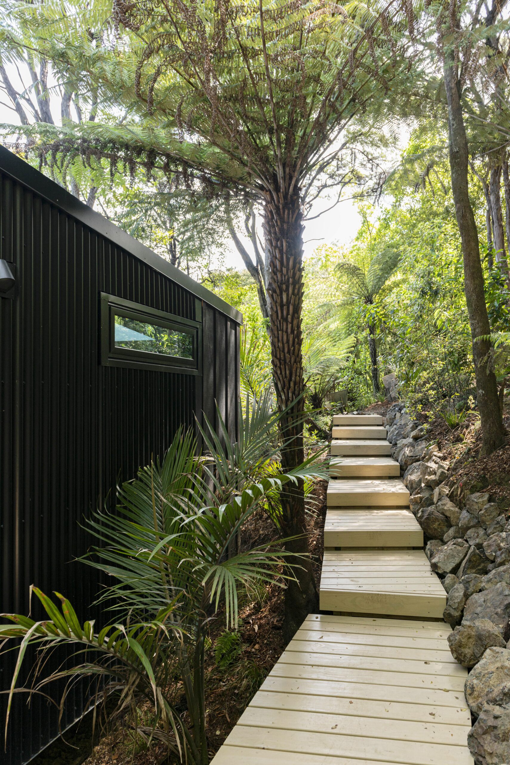 A house with black coloursteel, with a side timber path in the bush