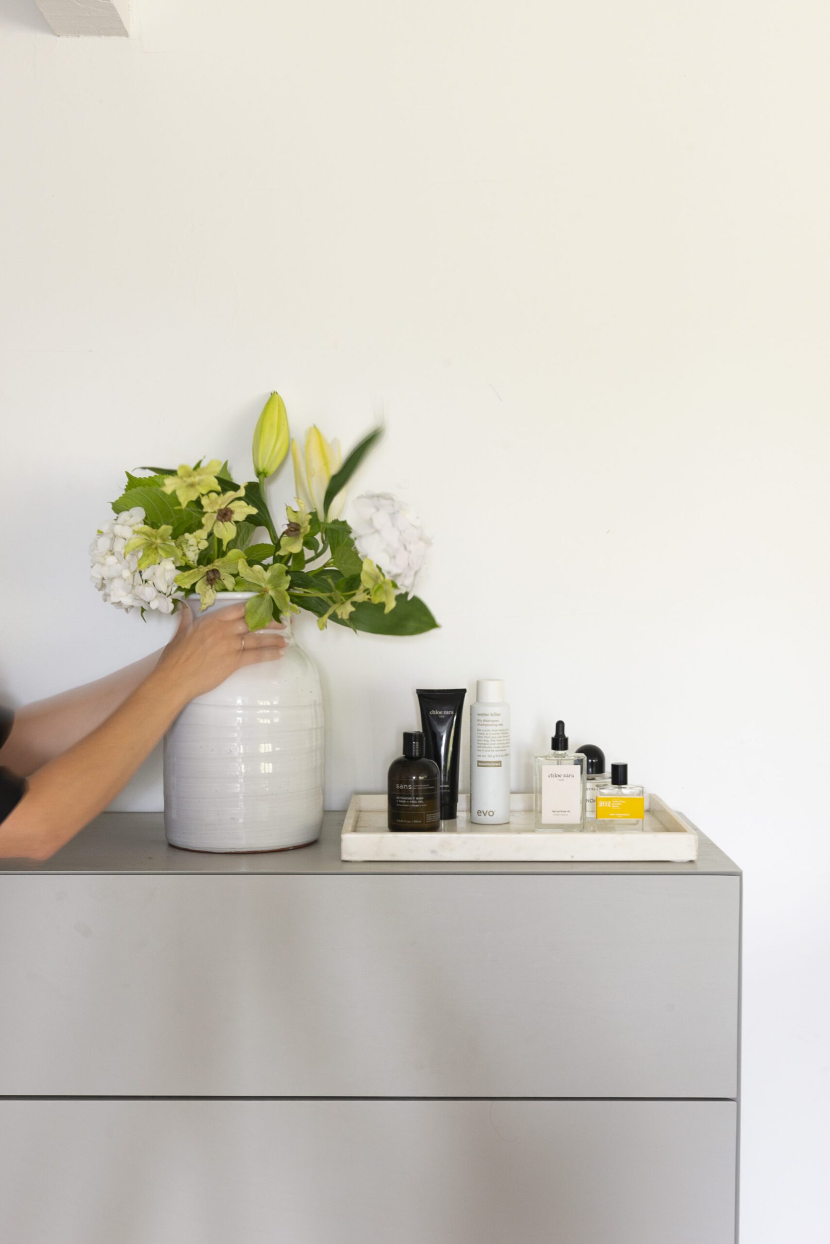 Claudia Zinzan arranging flowers in vase with perfumes beside it