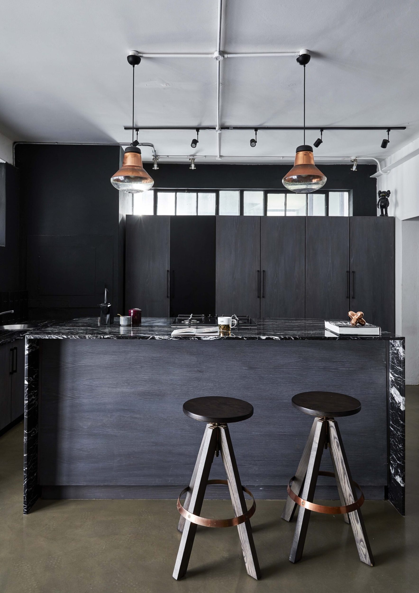 A black kitchen with white ceilings and brass hanging lamps