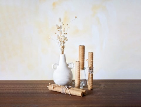 A white vase surrounded by honey candles