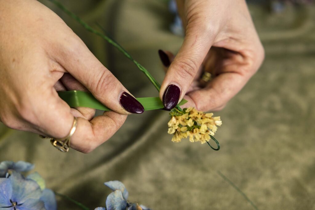 Hands using green tape to wrap flowers onto a wire crown