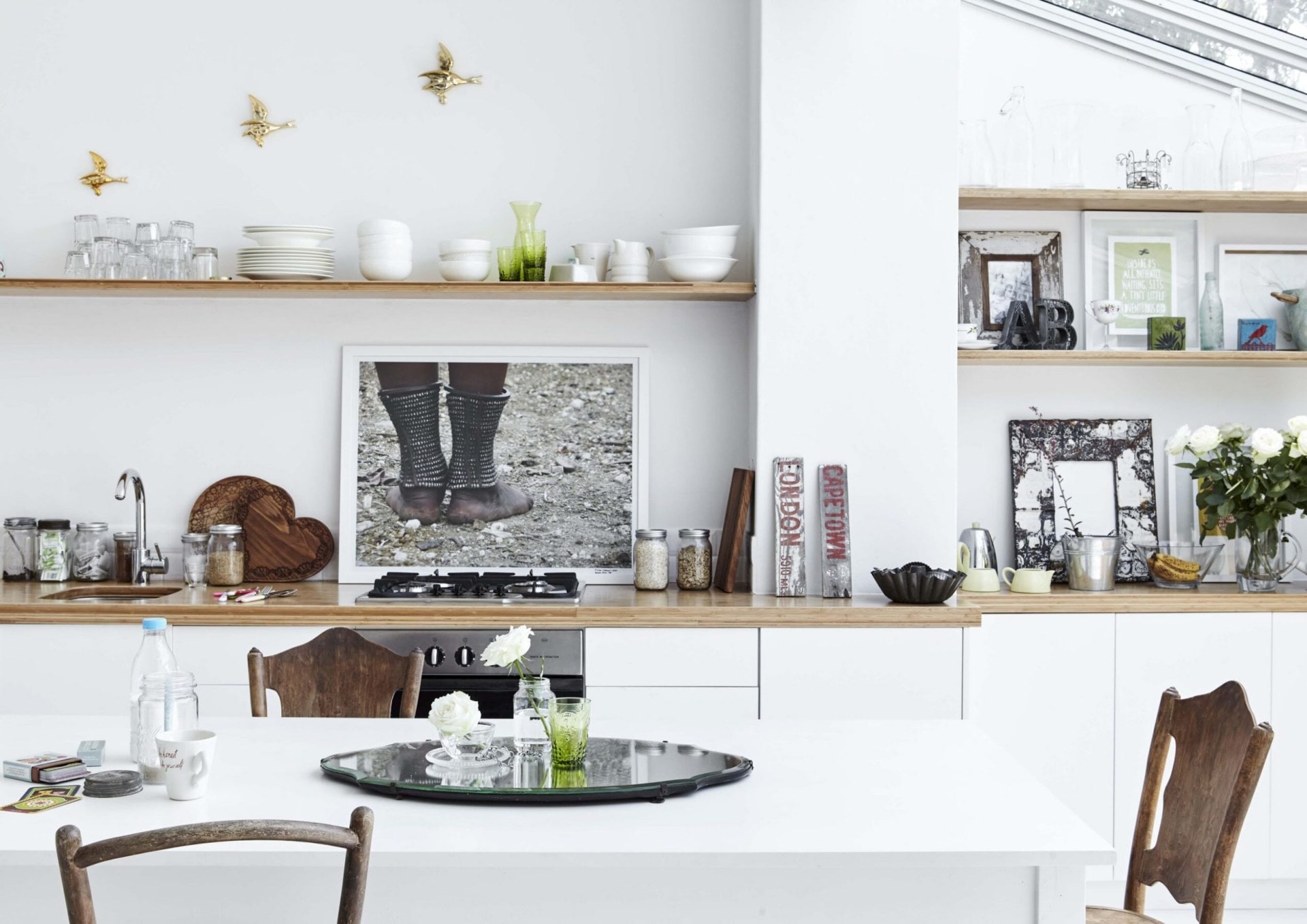 A kitchen with white walls, white cabinets and wood bench tops with assorted art on shelves in the walls