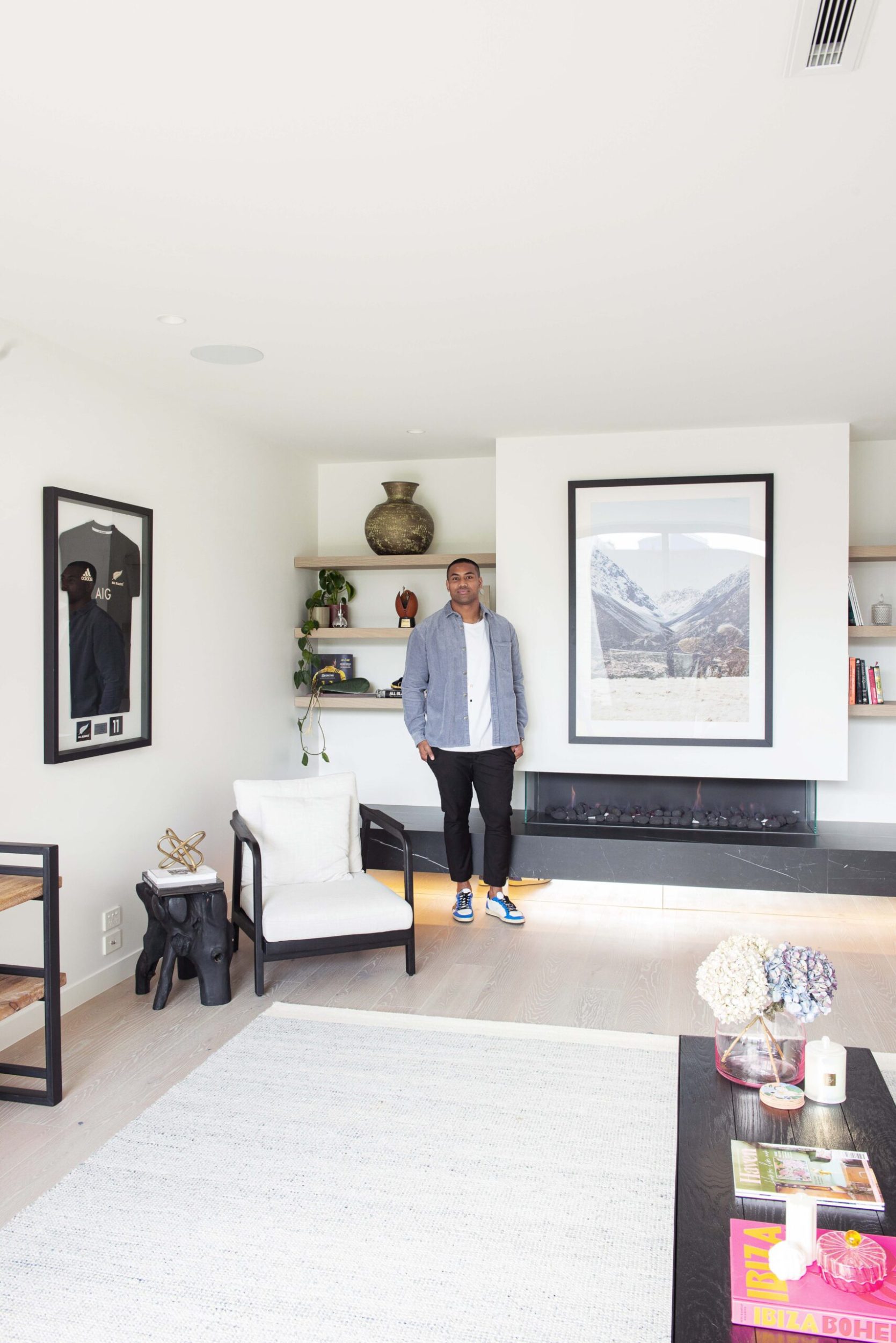 Julian Savea standing in his living room next to a All Blacks jersey in a glass frame