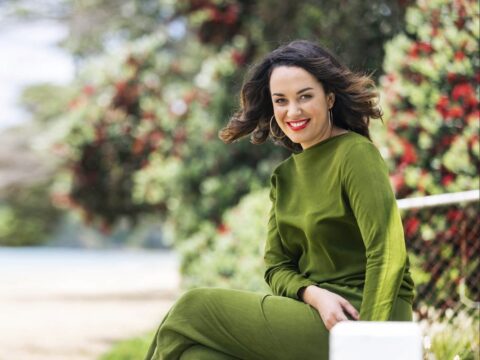 Kanoa Lloyd wearing green dress sitting by pohutukawa trees