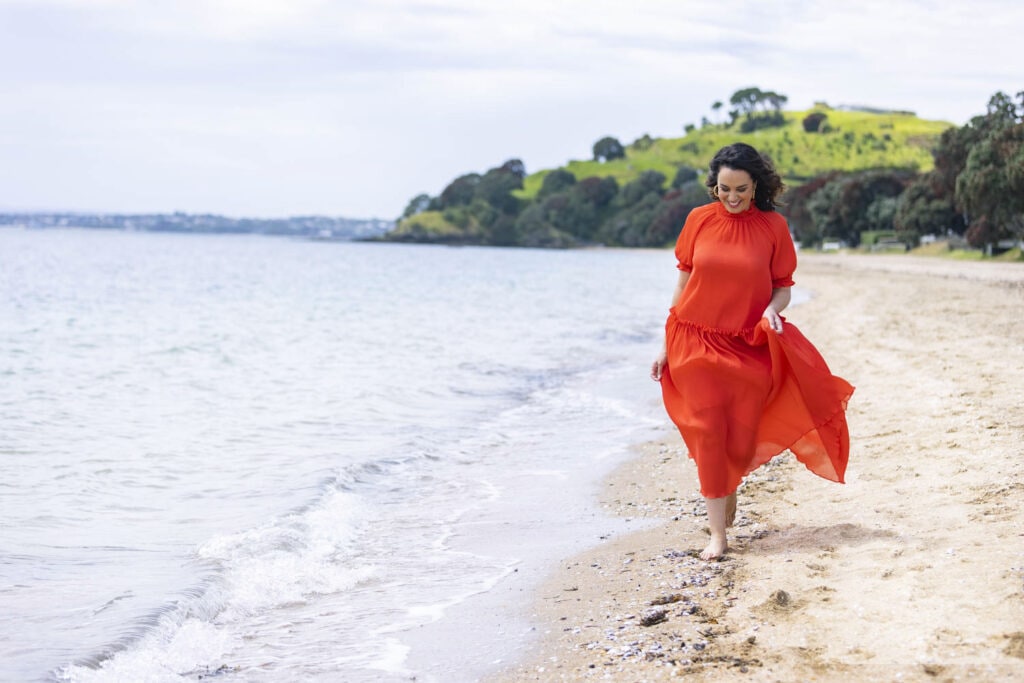 Kanoa Lloyd wearing red dress walking on beach