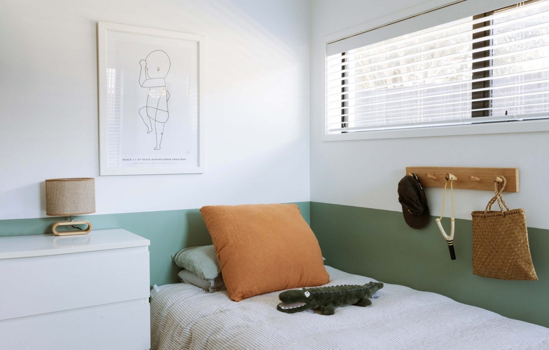 Child's bedroom with half painted wall in green, hooks on the wall and white and rust bed linen
