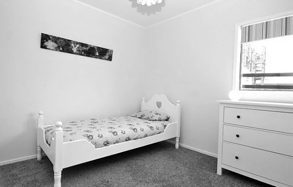 Black and white photo of a bedroom with white walls, grey carpet and a single kid's bed