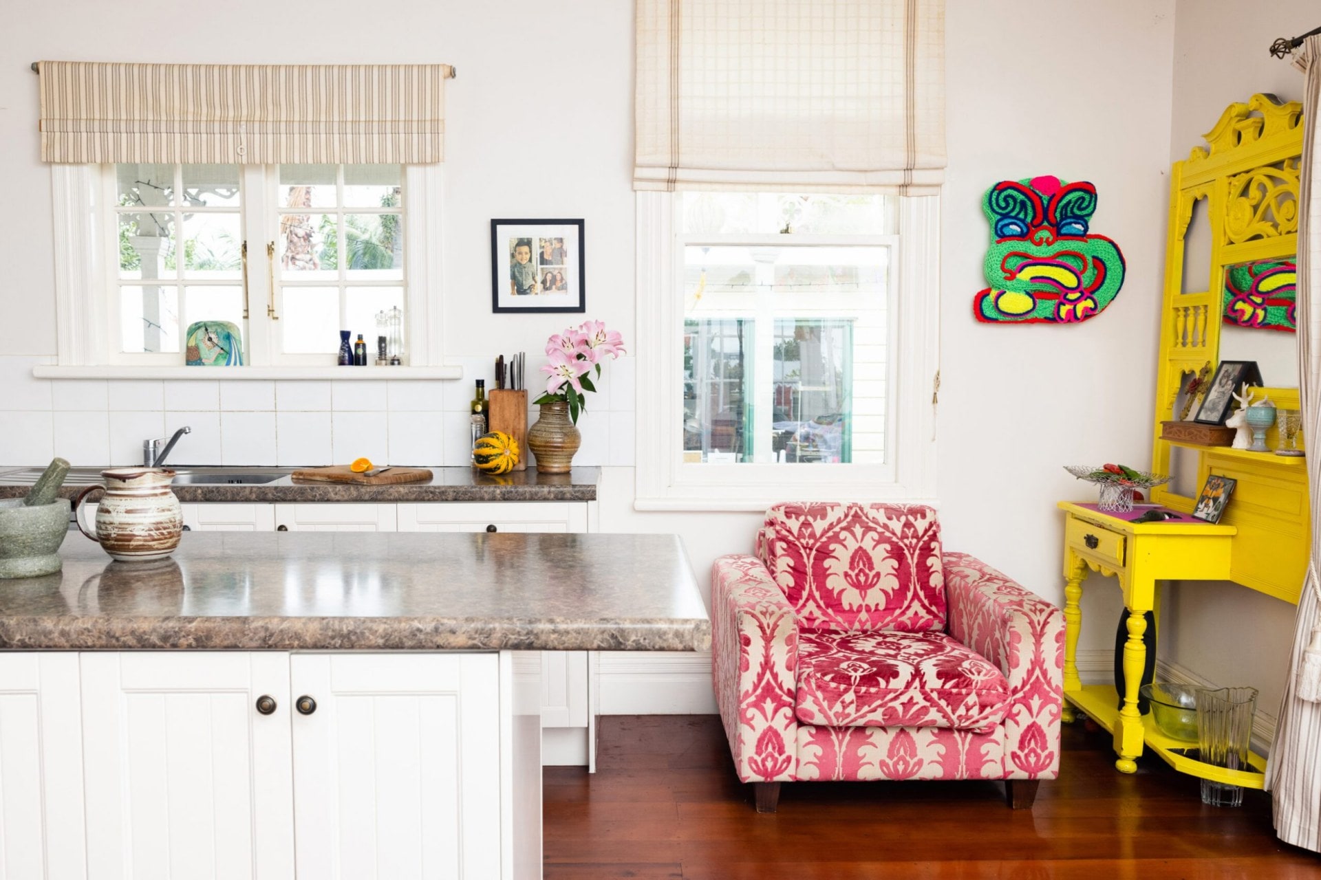 Kitchen with tall white walls, grey benchtop and a red armchair and yellow cabinet in the corner