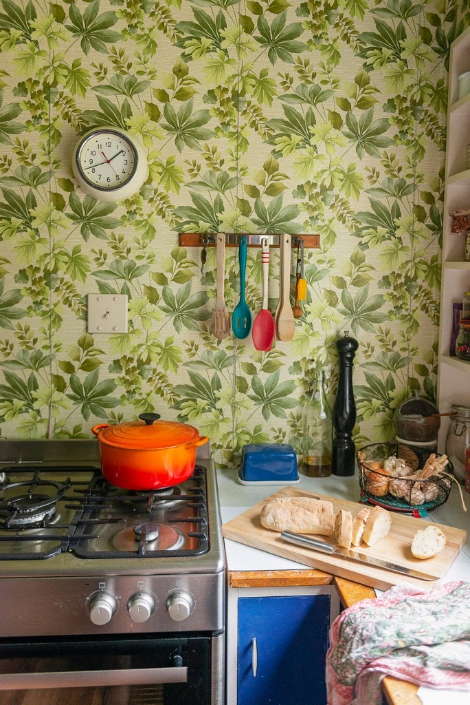 A kitchen with blue cabinets and botanical patterned green wallpaper