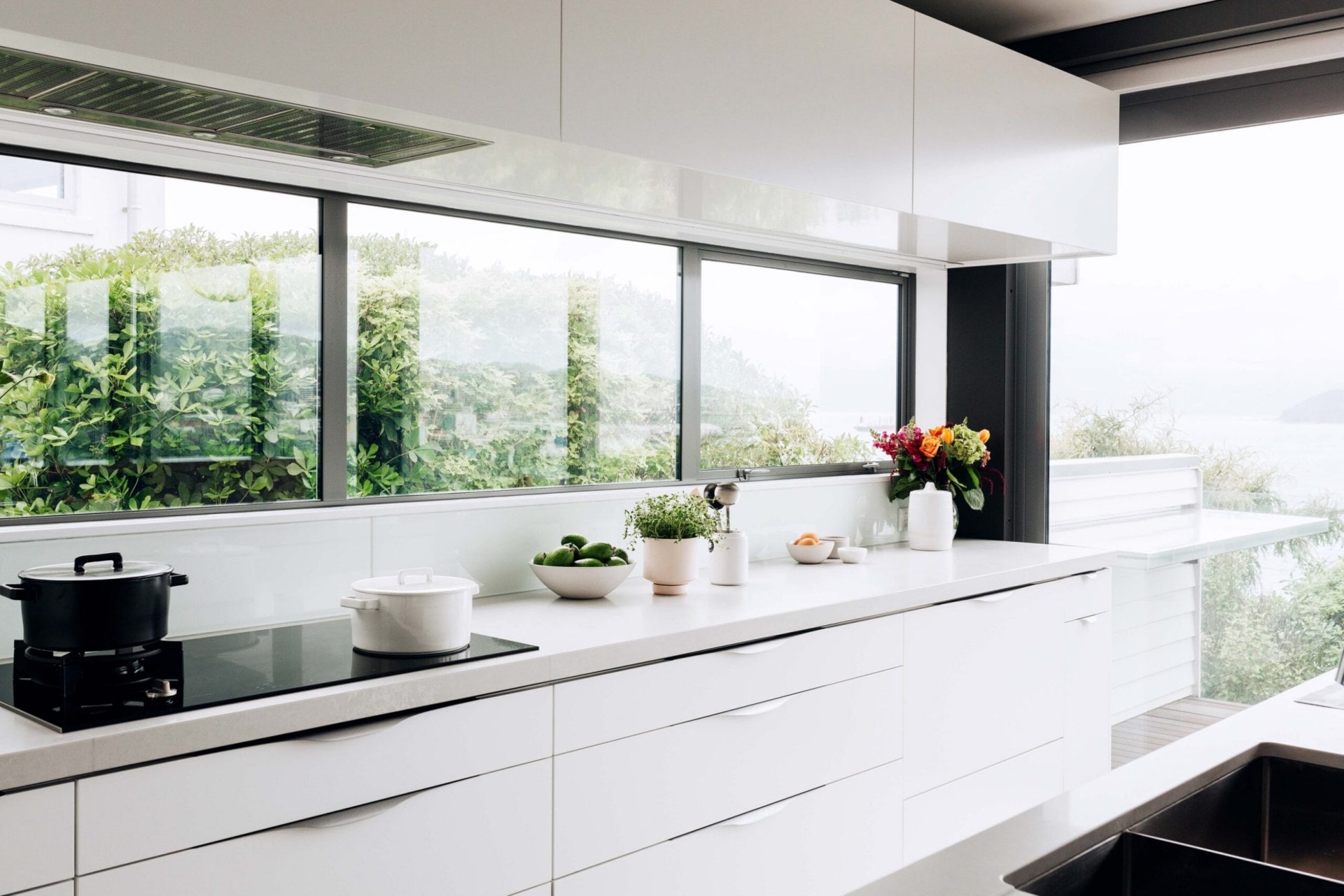 Kitchen with white cabinets, a white marble benchtop, black beams and large windows