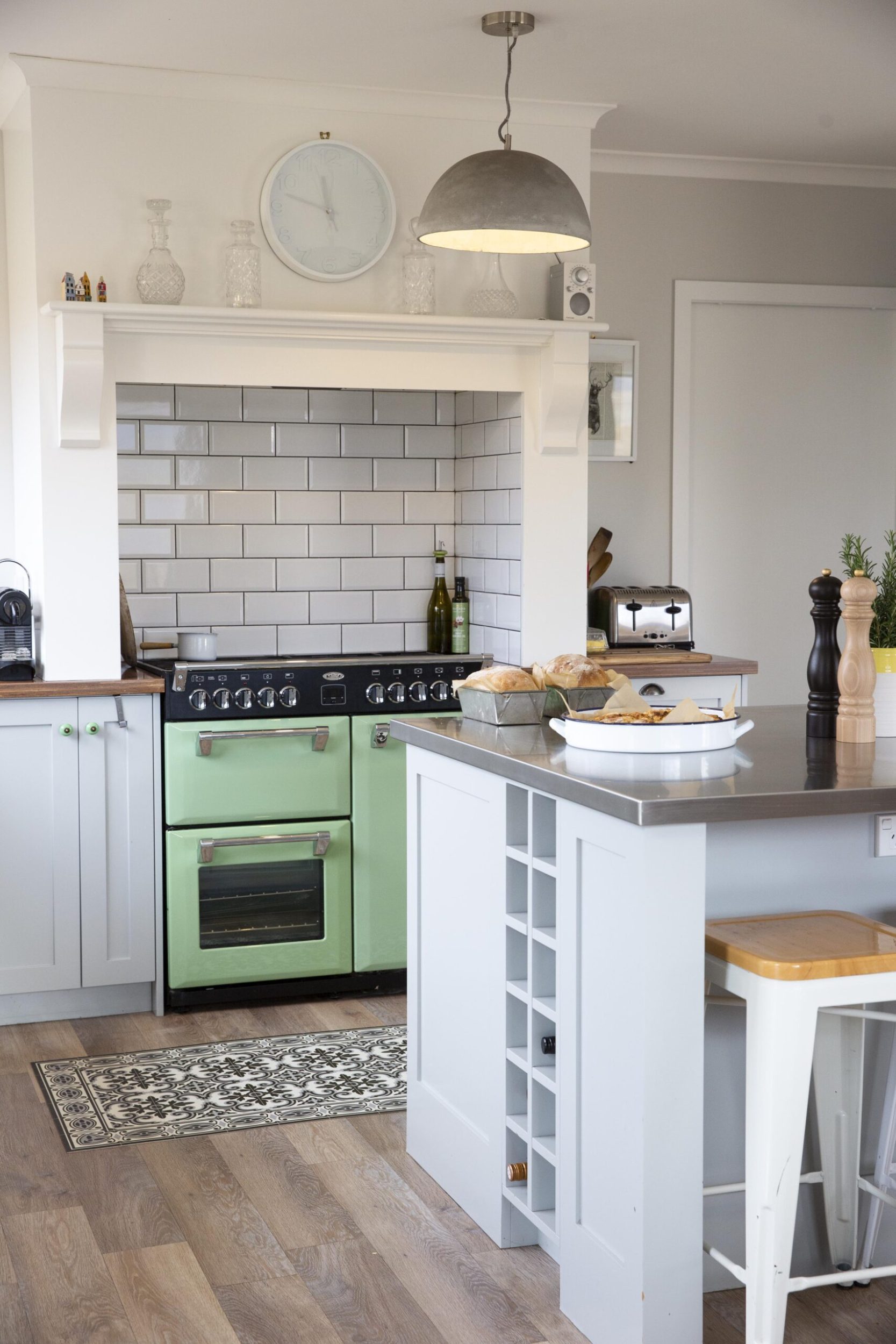 A kitchen with a silver bench topped island, subway splashback tiles and a green Belling range cooker