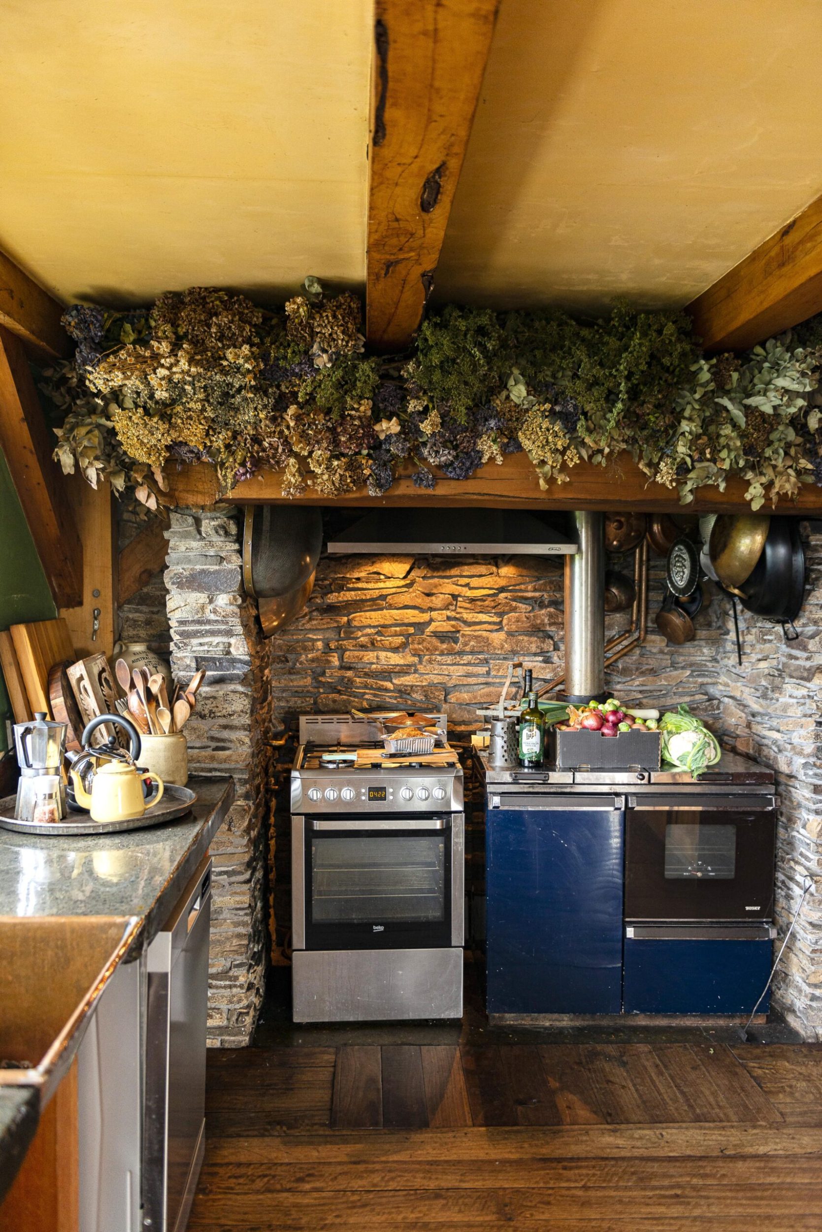 A cottage style kitchen with grey brick walls, polished wood floors and hanging flowers
