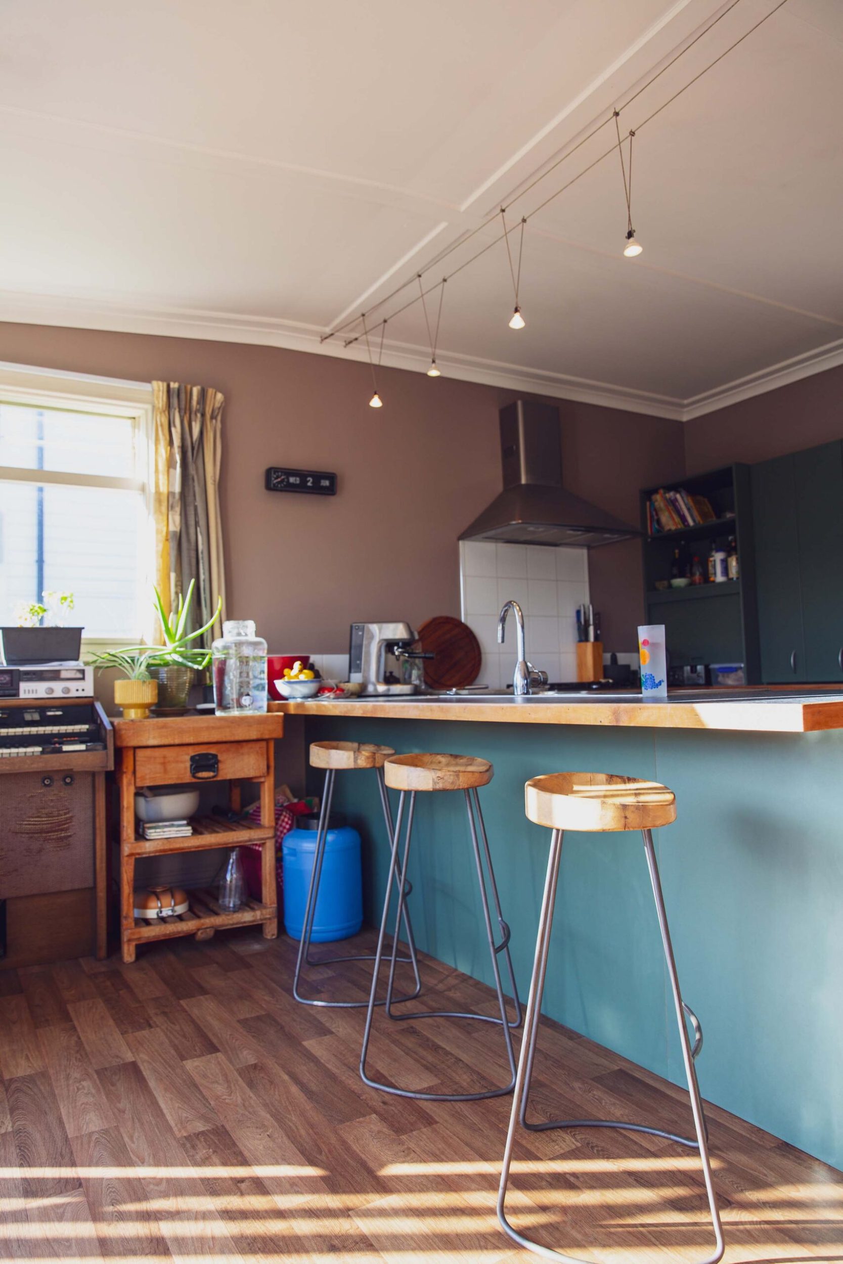 A kitchen with brown walls, a blue bench, hanging lights and round wood vintage stools