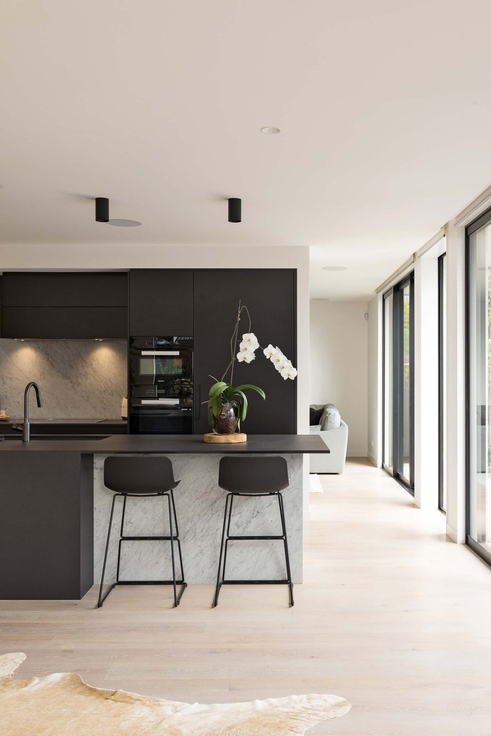 A kitchen with black cabinets, a stone splashback and black metal stools