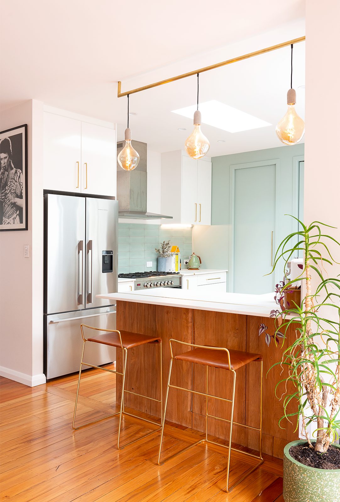 Renovated kitchen with wooden floors, hanging lights, teal splashback and drawers and a skylight