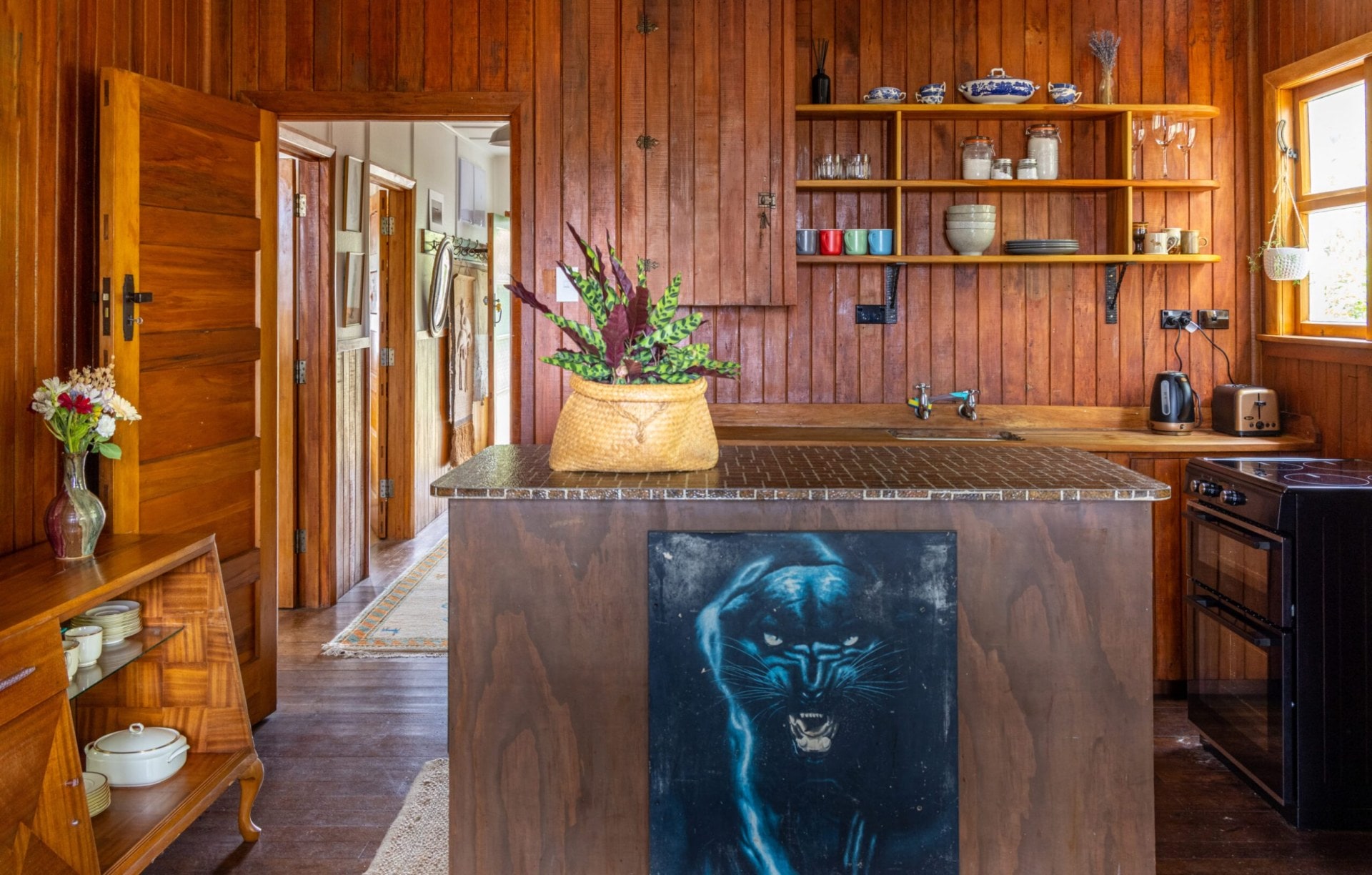A brown wood panelled kitchen with brown benchtops and a decorative black panther painting