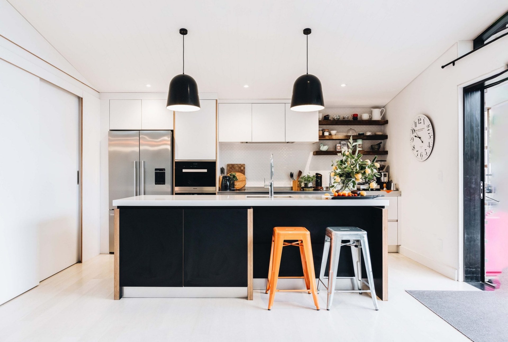 large kitchen with white cabinets, a black island, black pendants from the ceiling and floating shelves in the right corner