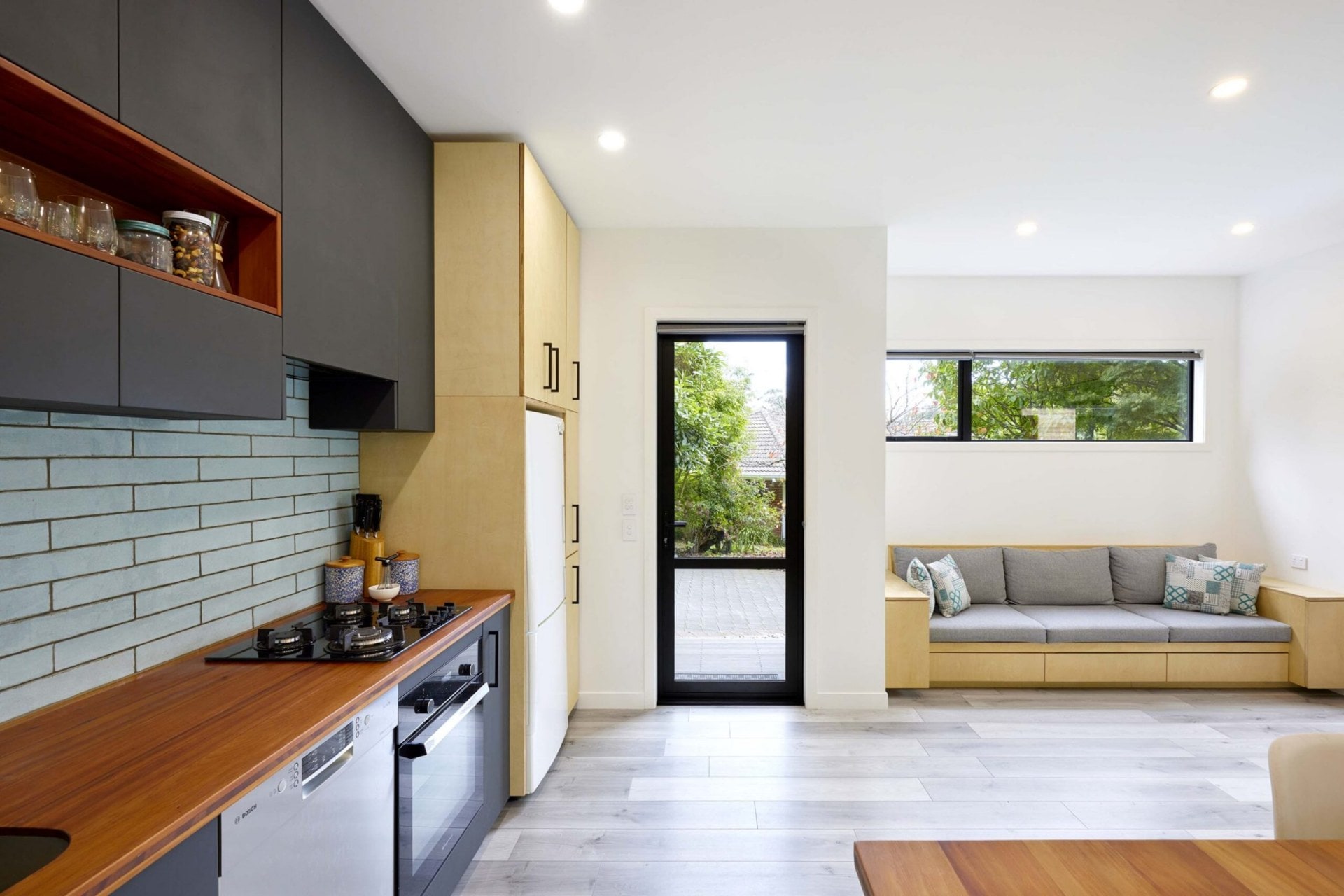 A joint kitchen and living room space with light wooden floors and green tiles