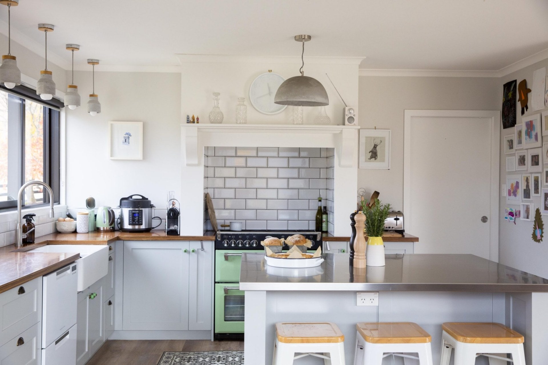 A white country style kitchen with a silver island, subway splashback tiles and hanging lights