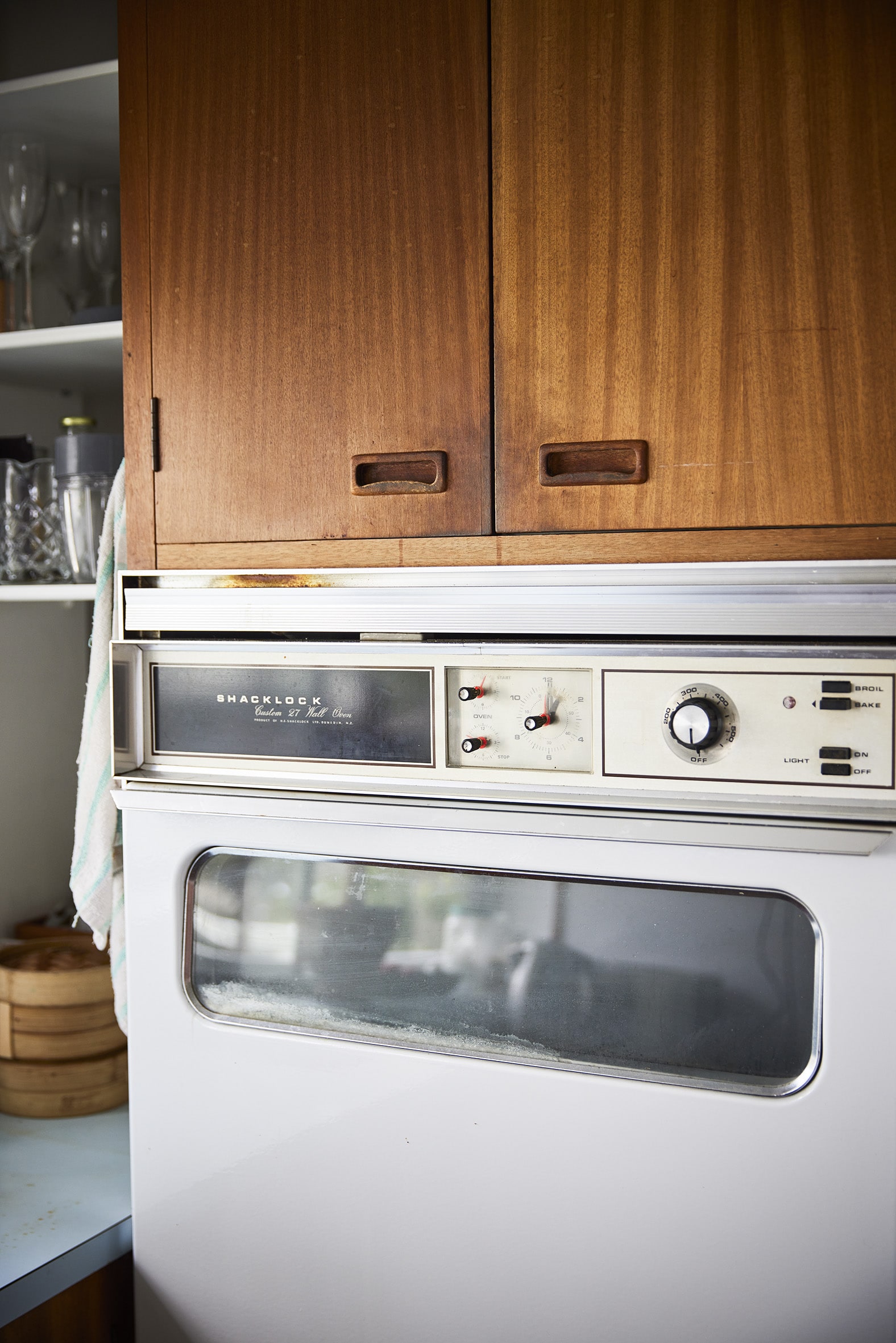 A mid-century white oven below wood panelled cabinets
