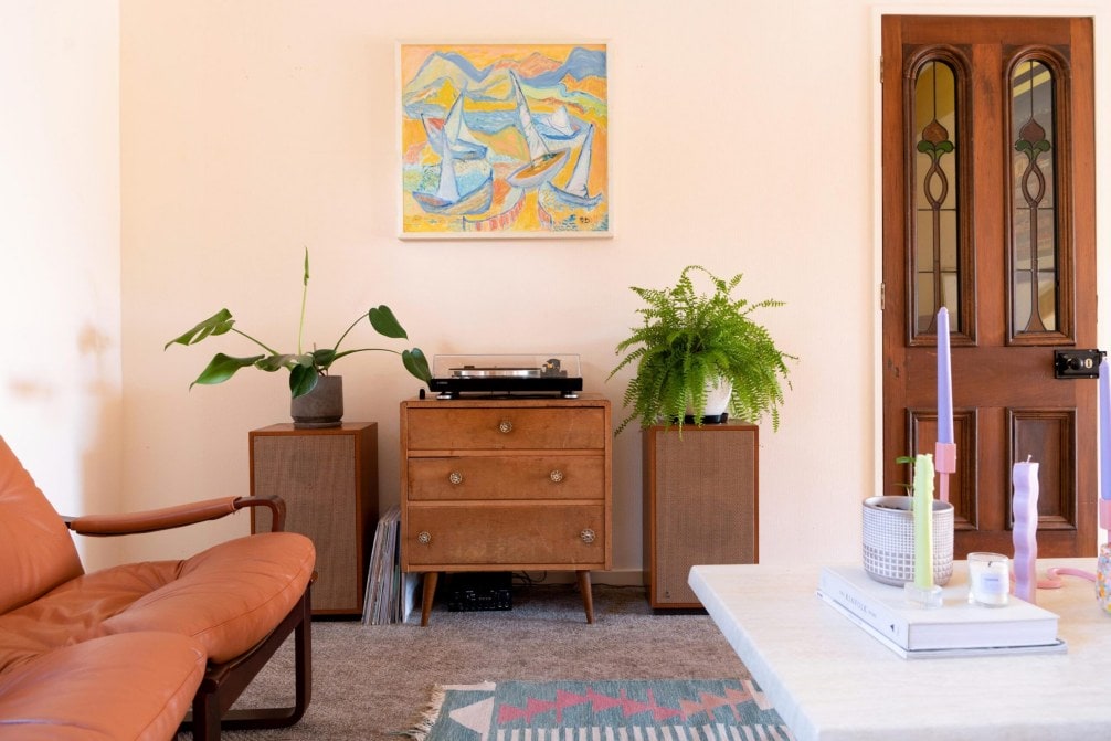 A living room with a brown couch, wood cabinets and speakers and decorative plants 