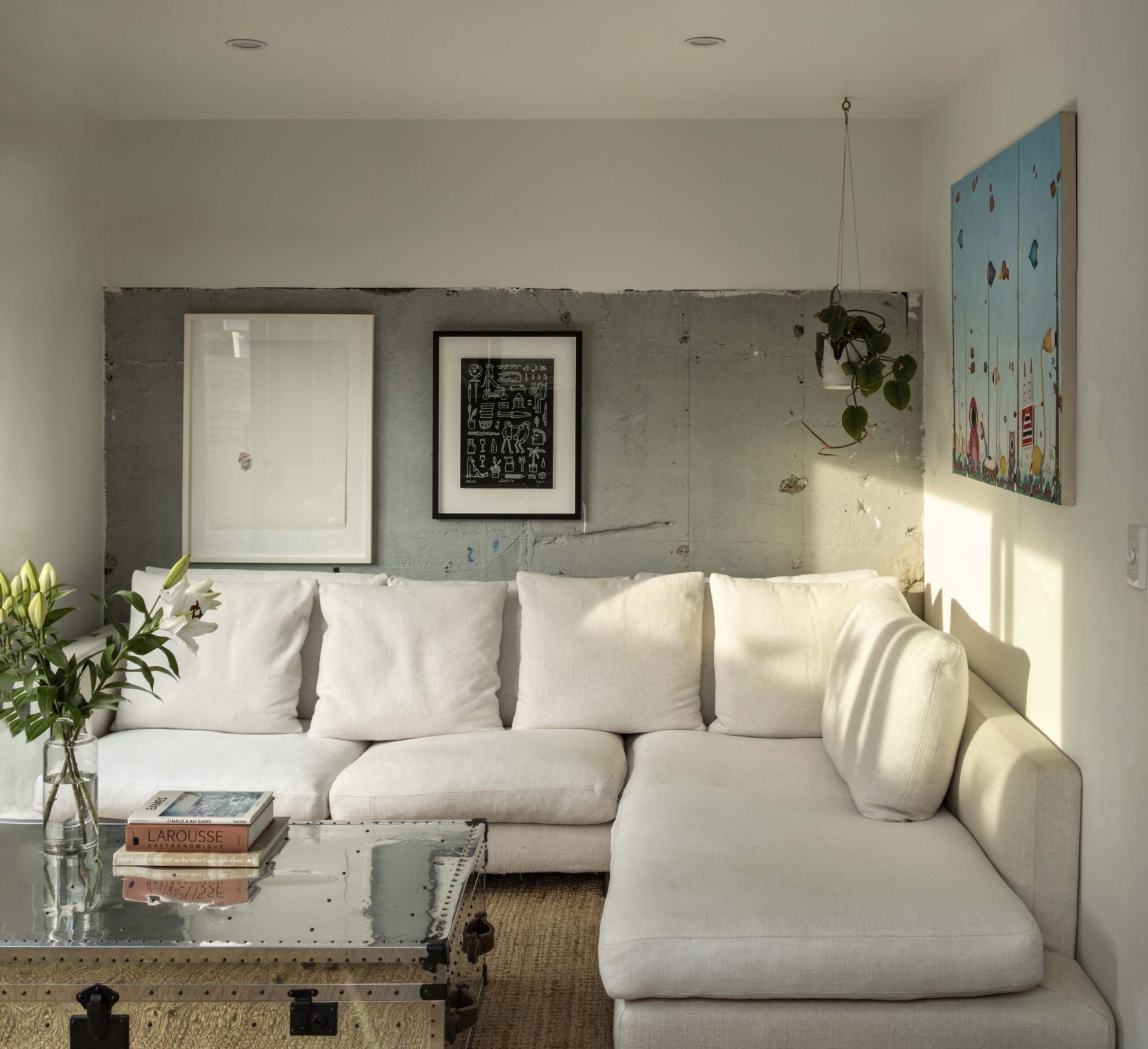 A living room with a white couch, a white and exposed concrete wall and a coffee table made out of a silver chest