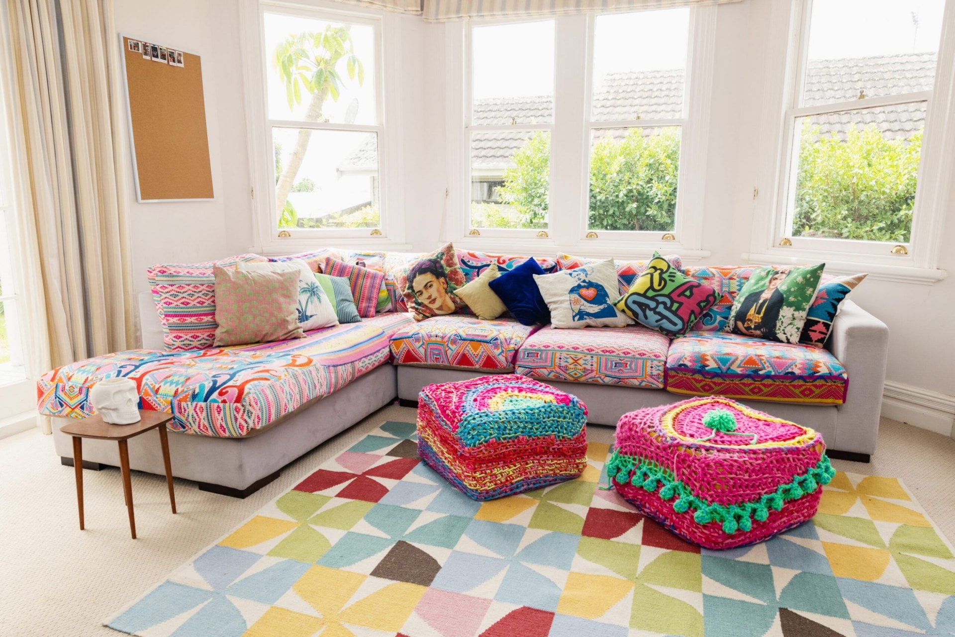 A living room with a grey curved couch covered by colourful crochet