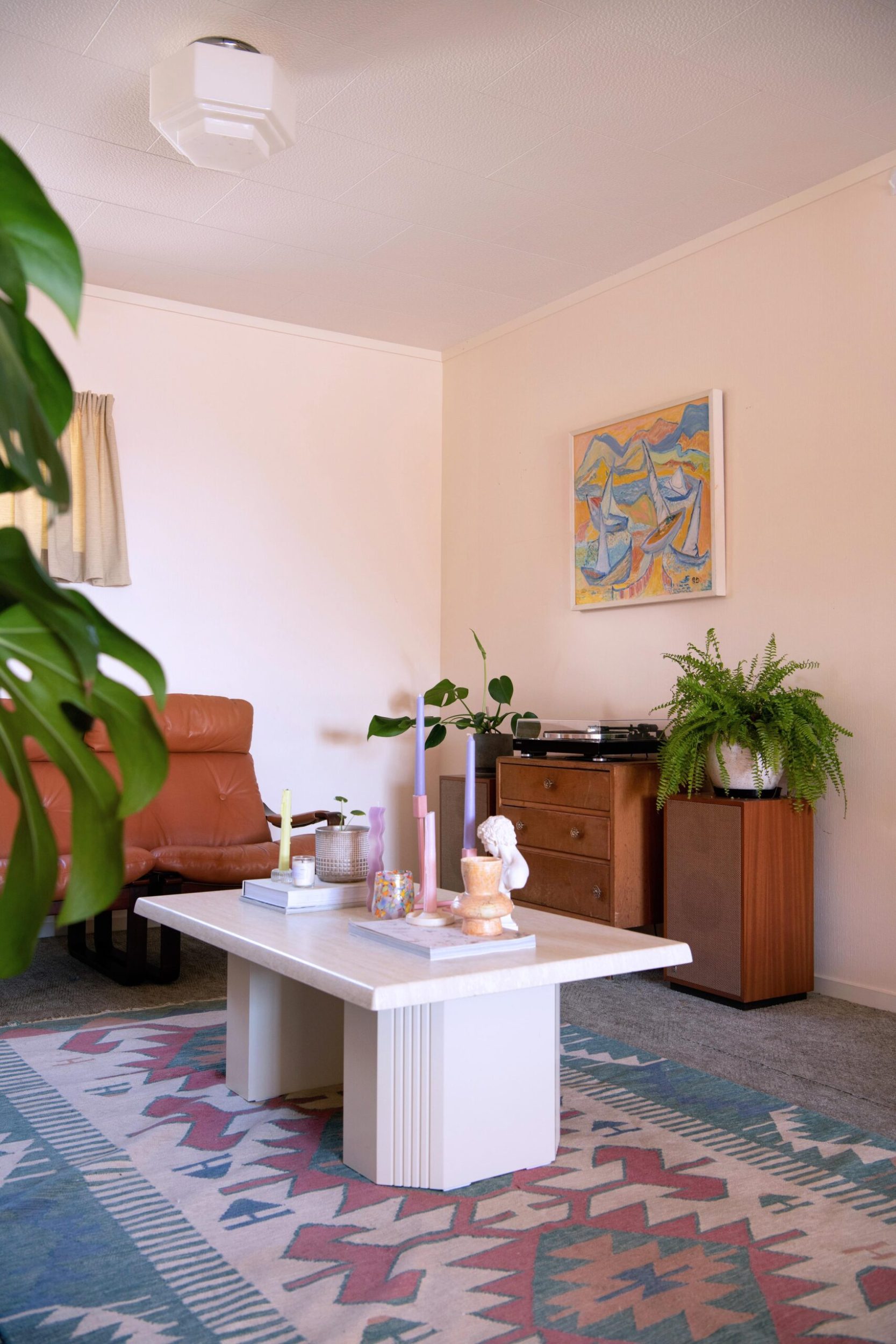 Living room with geometric rug, wood cabinets and blue table and monstera plants