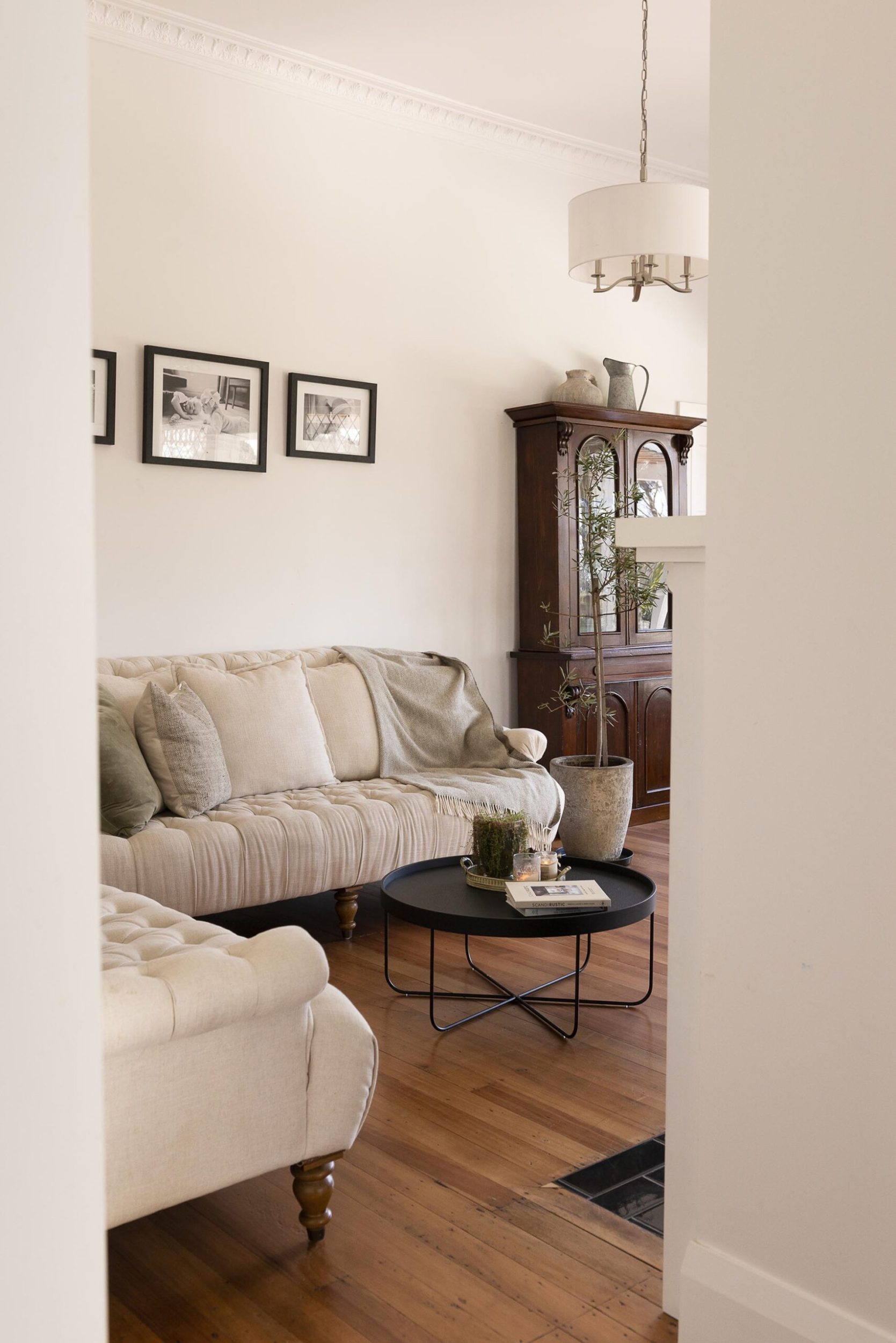 A living room with polished wood floors, white walls, a curved French style couch and vintage French antique armoire