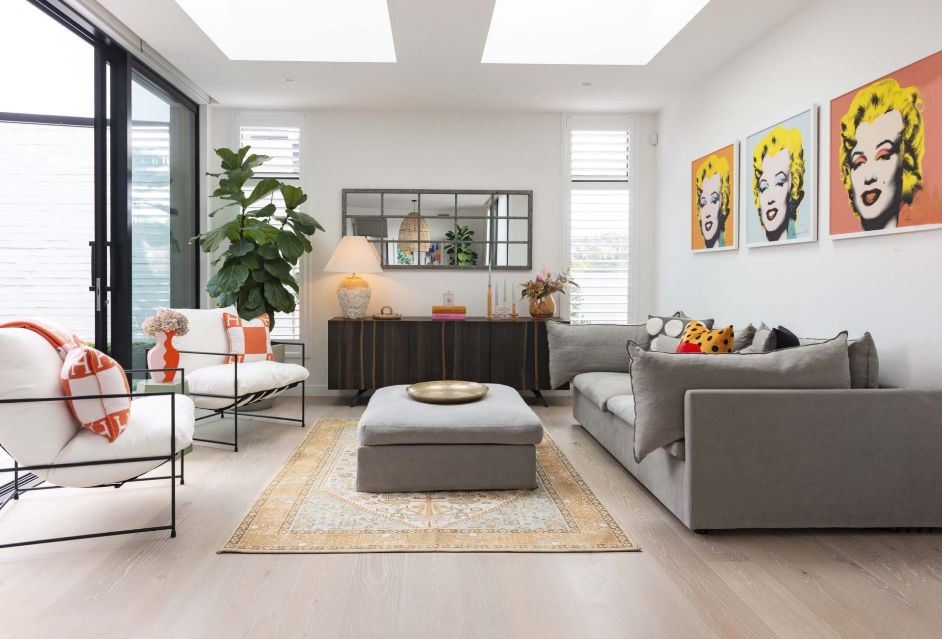 lounge room with a large grey sofa and white chairs, with pop art on the wall and a wooden sideboard at the back of the room