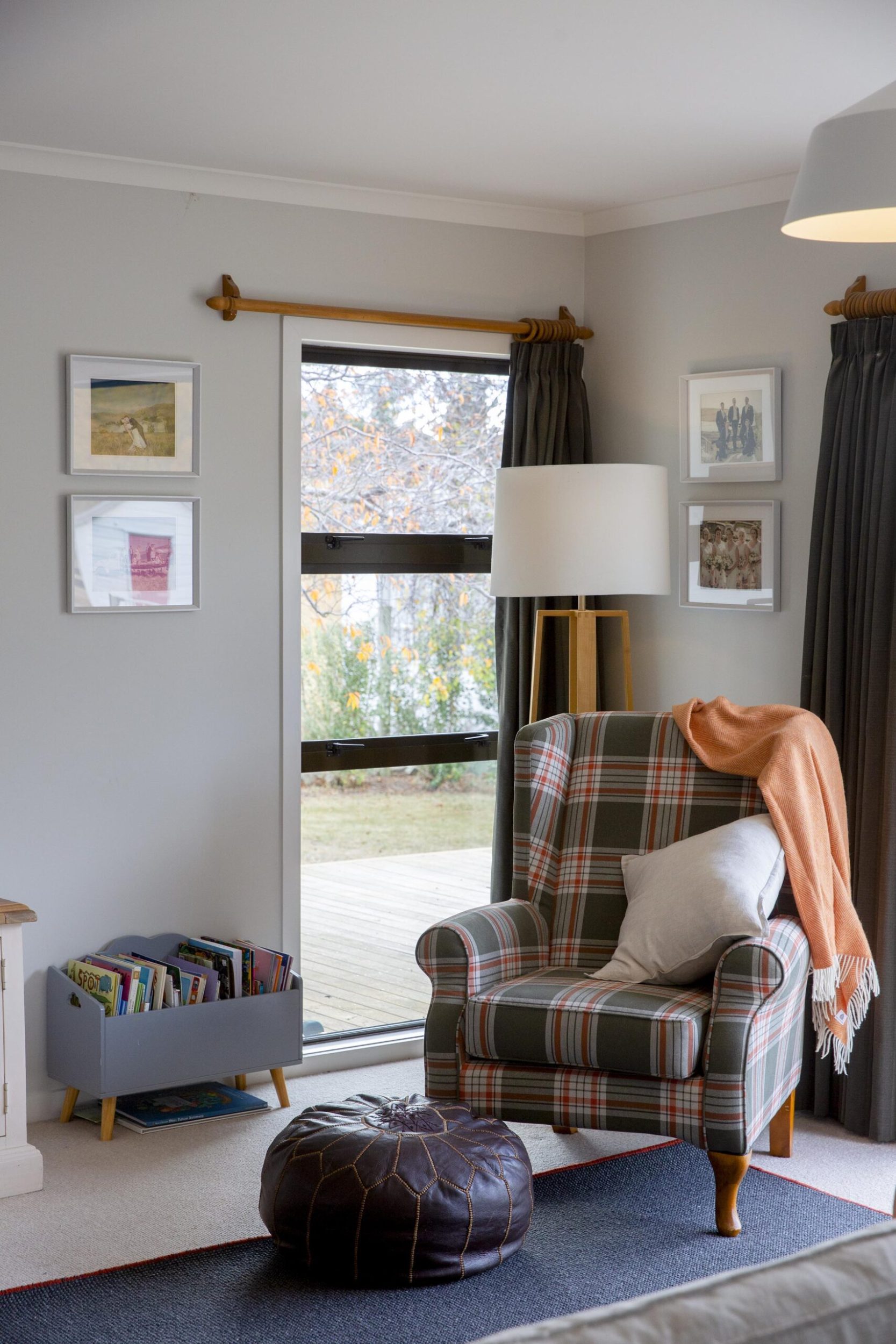 A living room with a tartain chair and an orange throw on top 