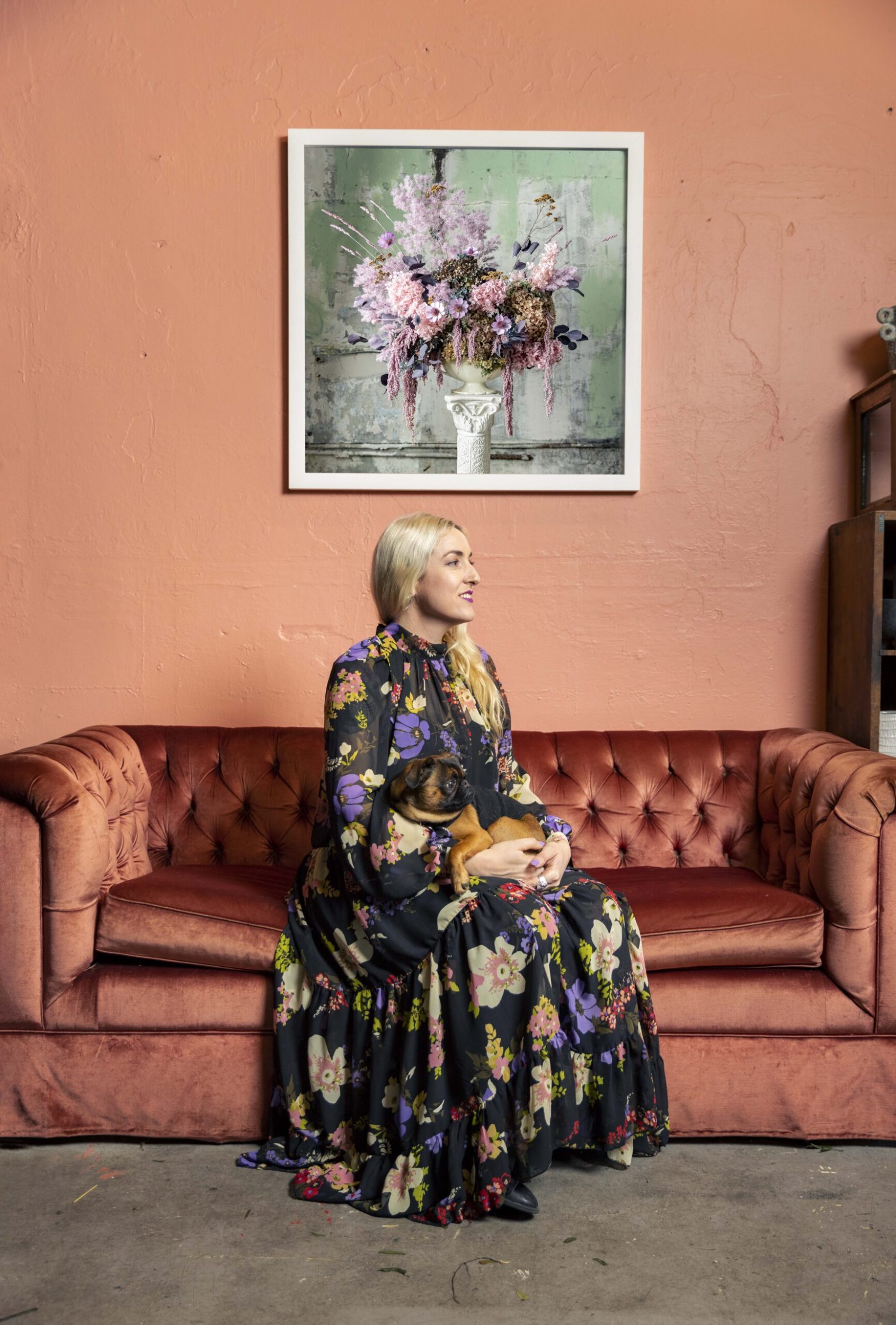 Georgie Malyon sitting on a velvet coral orange couch with her dog 