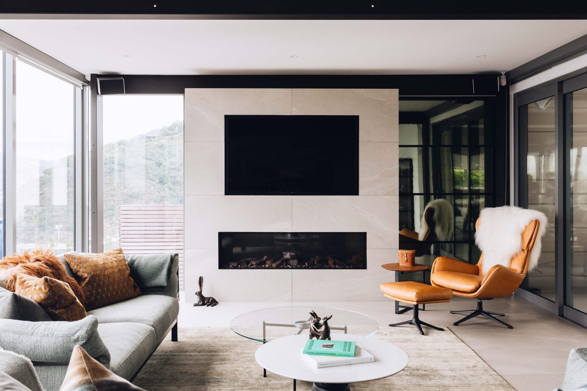 Living room with a grey couch, coral chair, a fireplace and large TV embedded within the wall