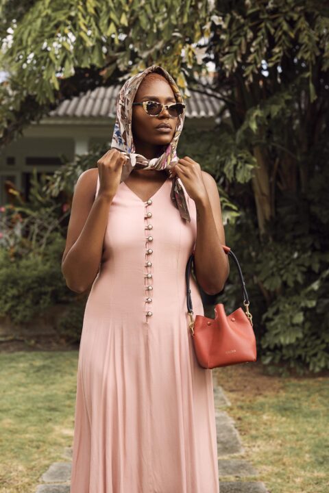 A woman wearing a floral head scarf, pink buttondown dress and orange Kaiso handbag