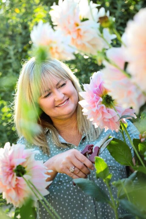 Lynda Hallinan smiling while holding cutting shears in a field of dahlias