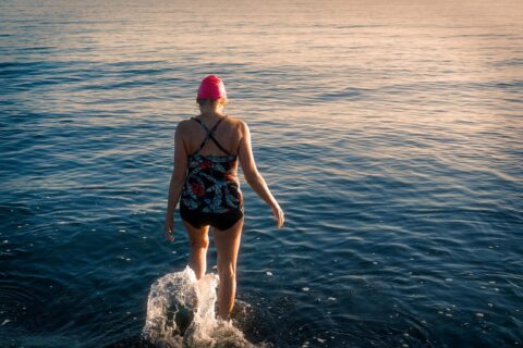Woman wearing a swimsuit and swim crap walking away from camera in the water