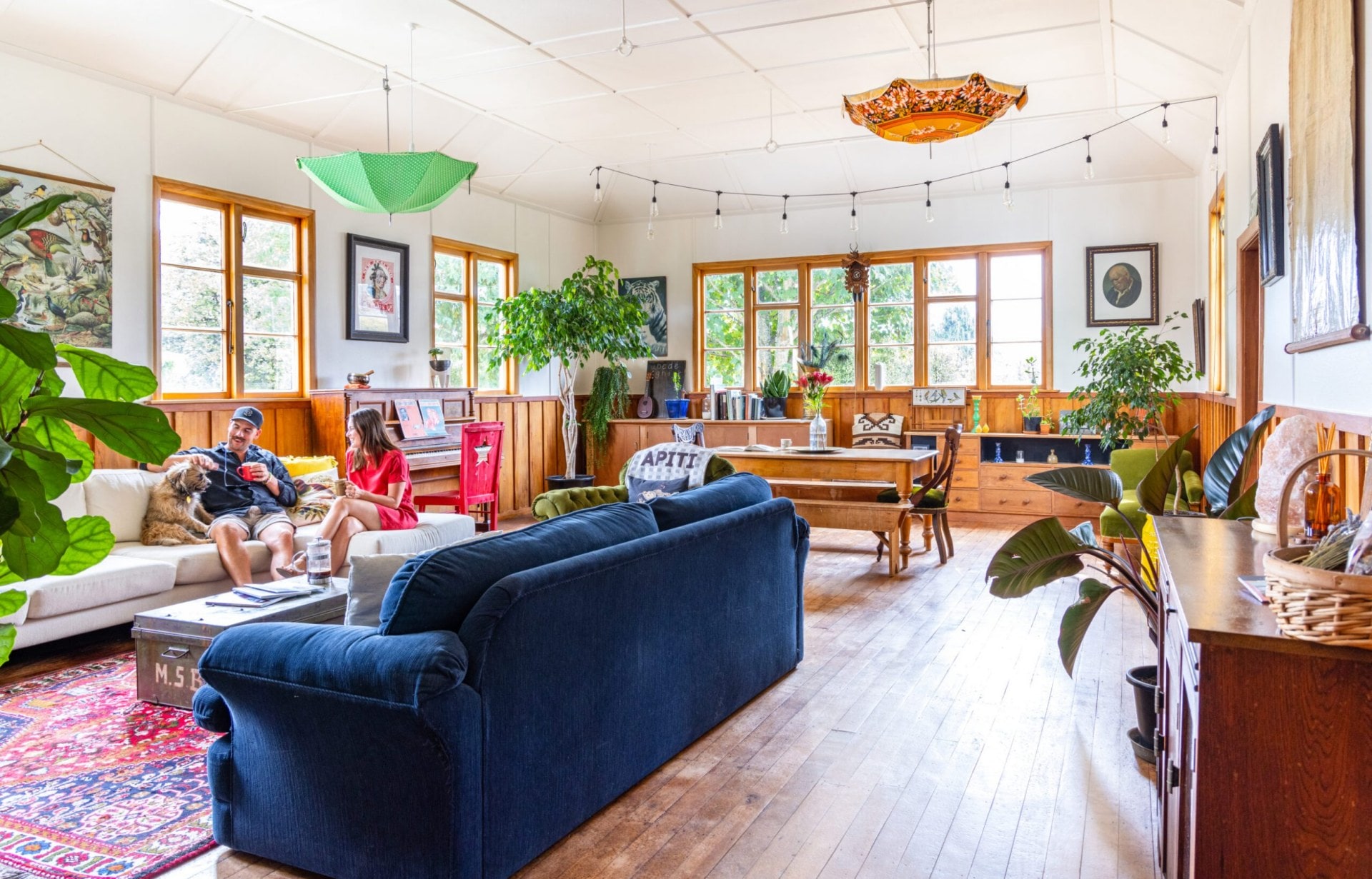 Jemma and Alex Robertson sitting in their living room with pet dog. The room has wooden floors, white walls and colourful hanging umbrellas as decor