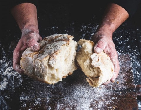 A close up of hands tearing apart loaf of white bread