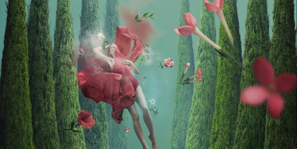 Woman wearing red dress floating in an underwater dream scene of forests and red flowers