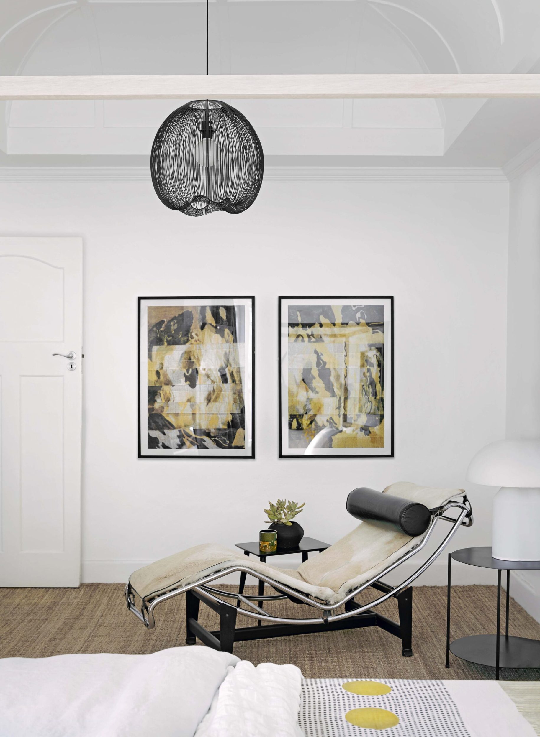 White room with wood floor, white walls, a round black lamp and two abstract artworks in black frames