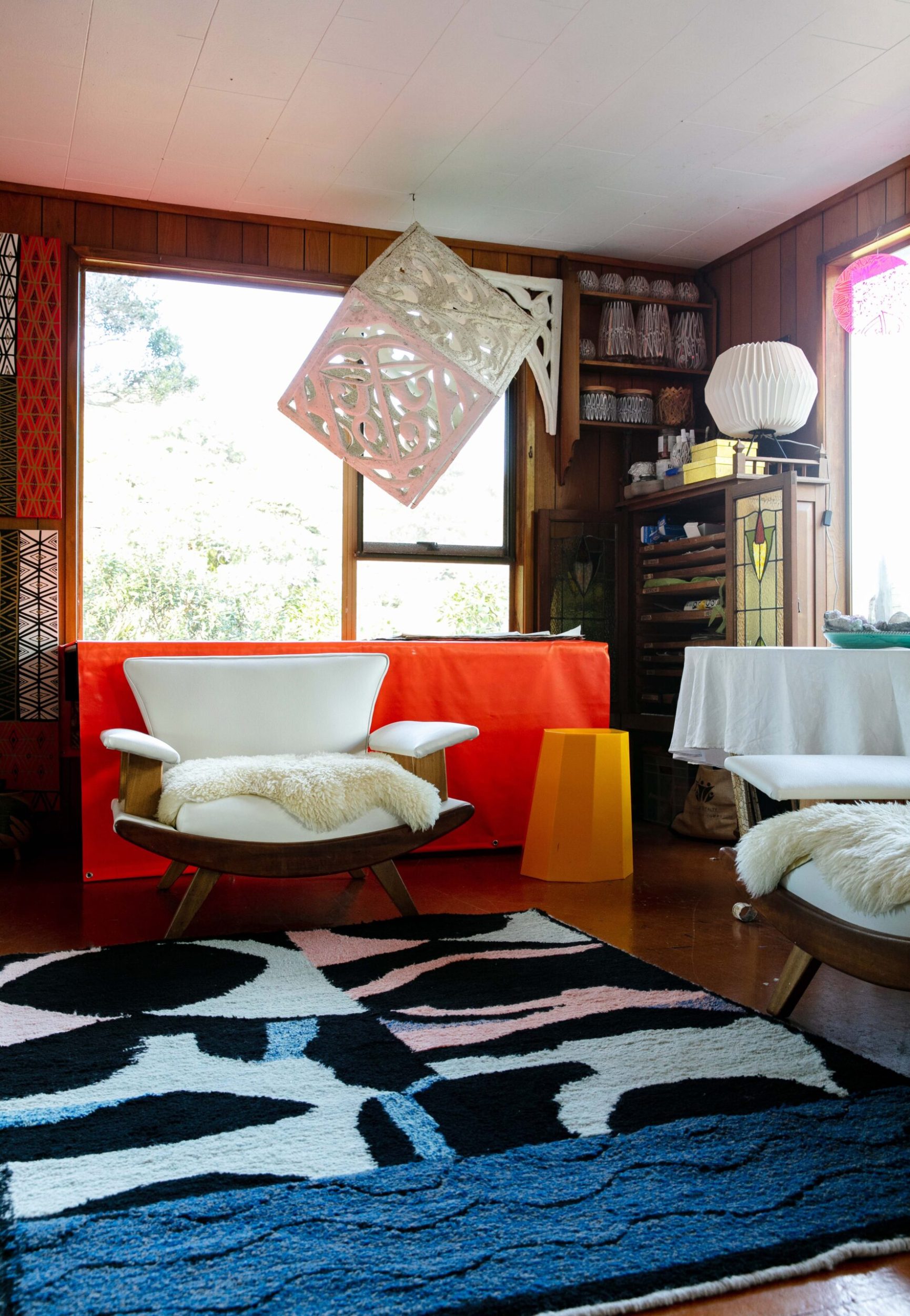 A living room with a blue, black and white patterned carpet, a white chair and couch and a hanging Metatron’s cube