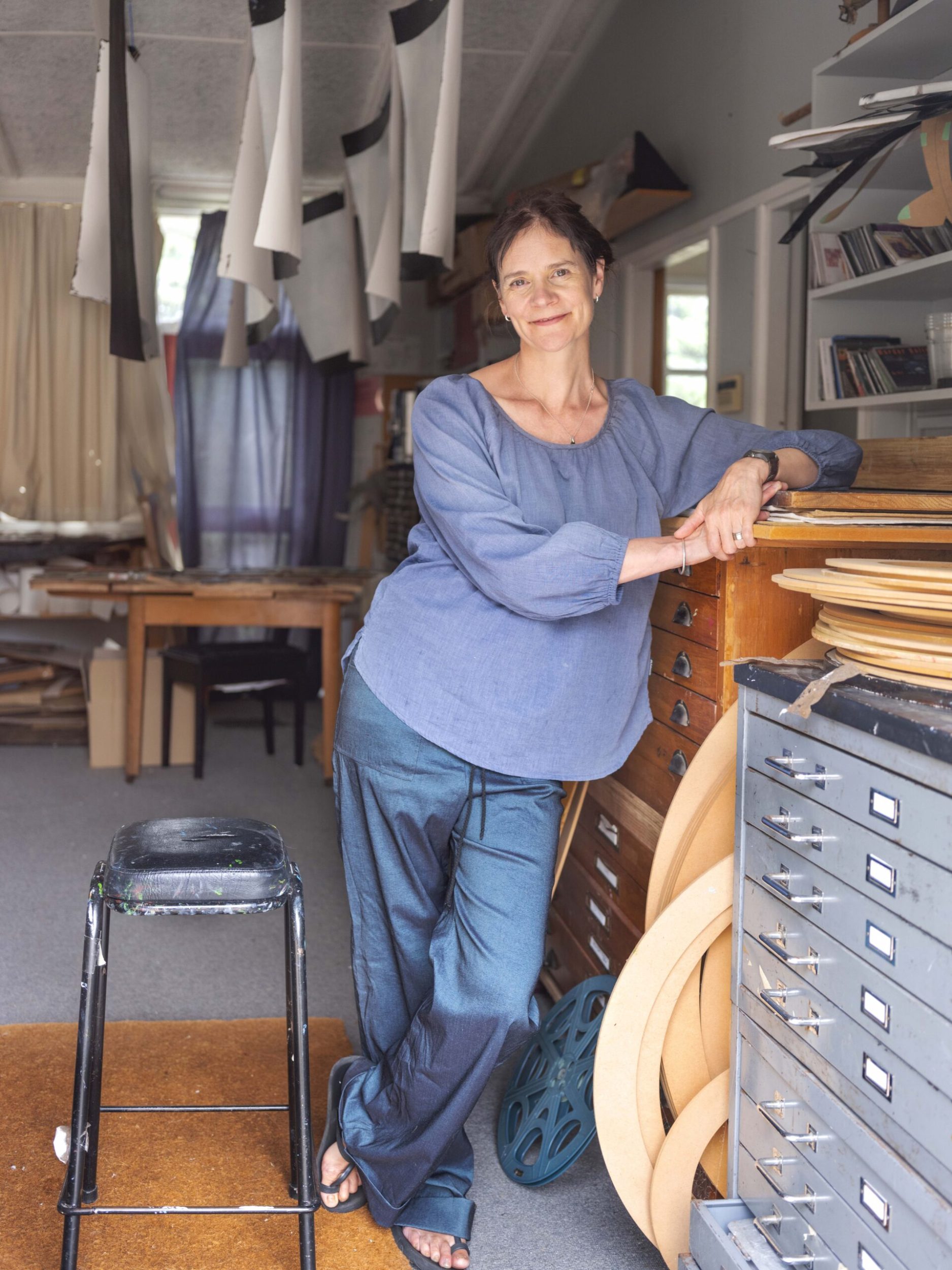 Artist Michele Bryant standing in workshop wearing blue top and jeans