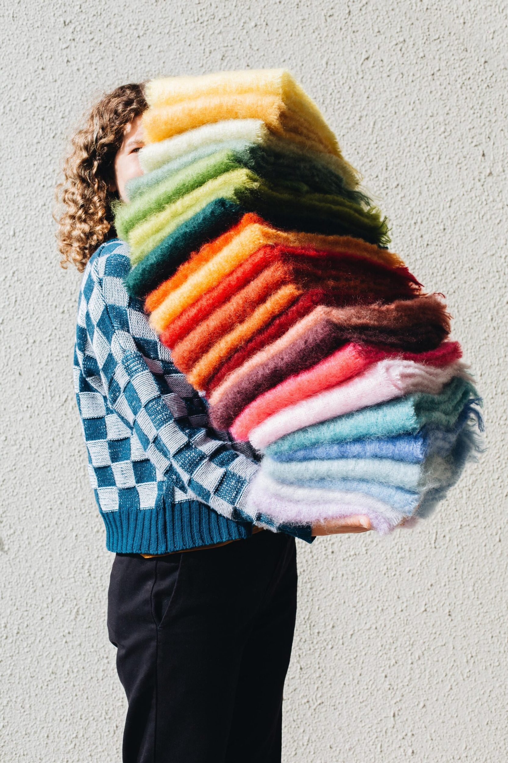 Fashion designer Millie Askew holding a tall stack of colourful textiles