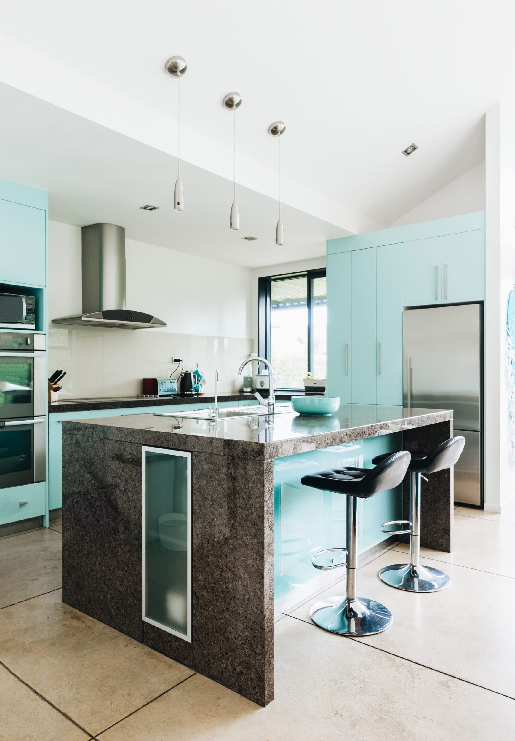 A white kitchen with mint green cabinets and a brown marble island