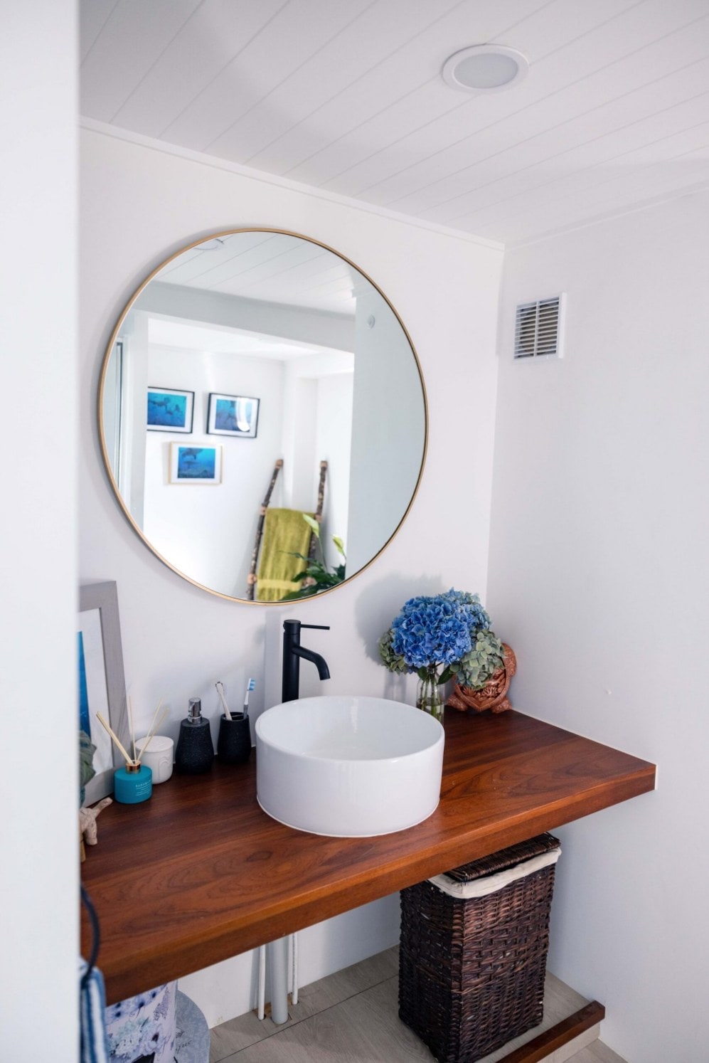 A bathroom sink with a brown cabinet and round gold mirror