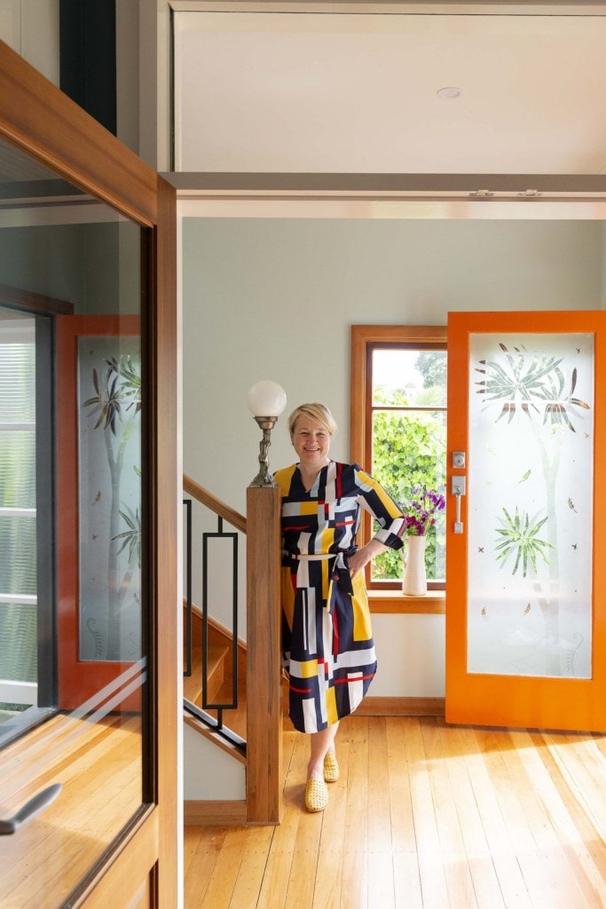 Ann Hay stands next to art deco staircase and orange front door