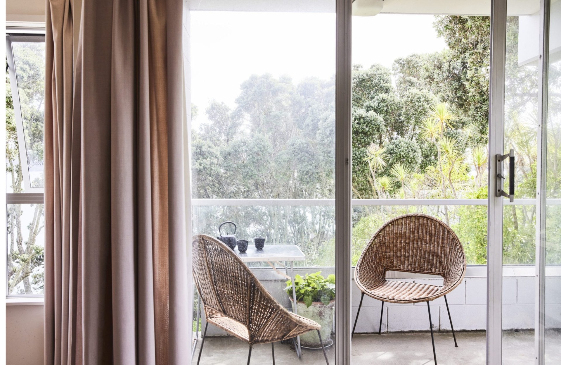 Open glass doors showing small deck with glass railing and two rattan chairs 