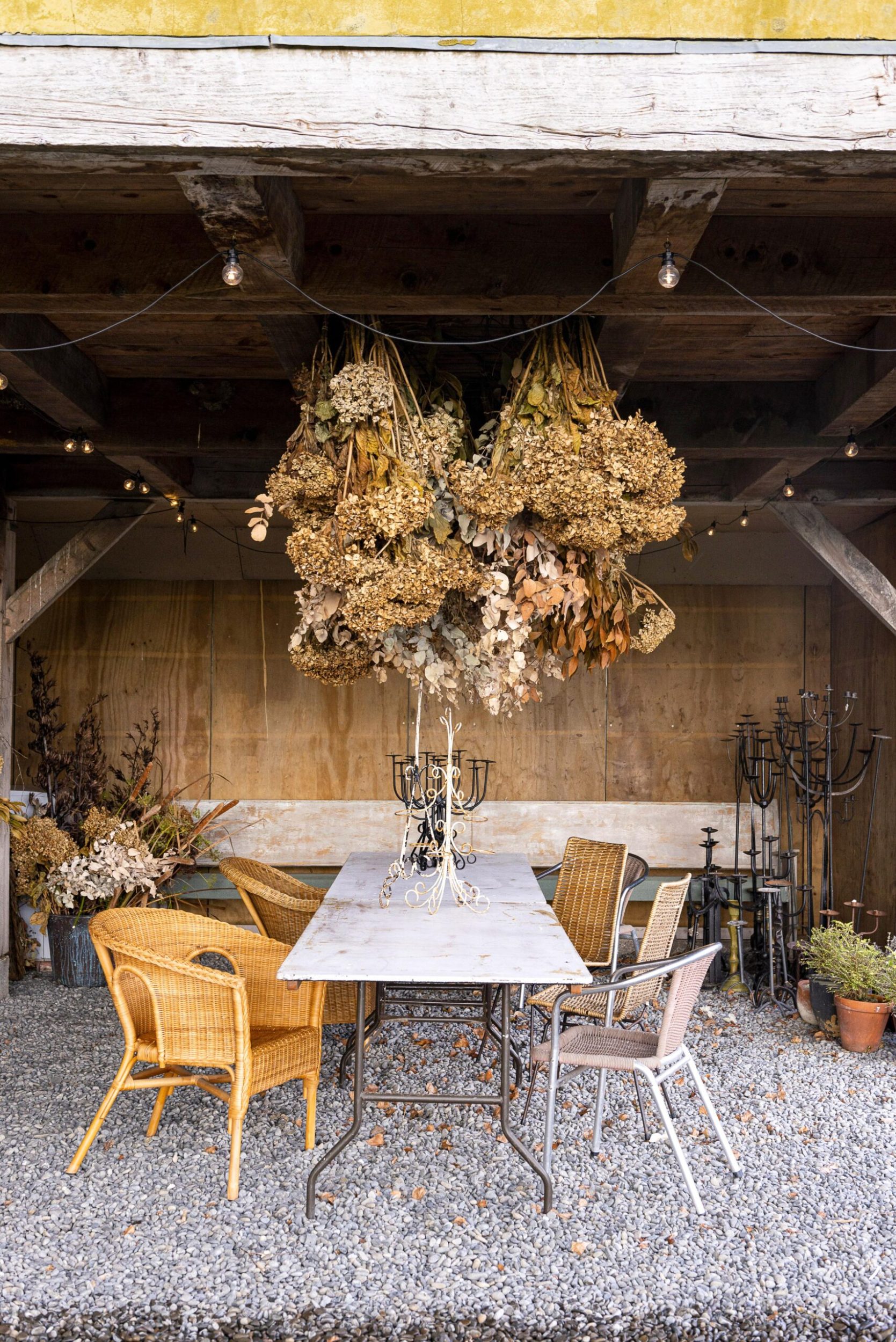 A rustic outdoor pavilion with a grey rock floor, marble dining table and large dried floral hanging arrangement