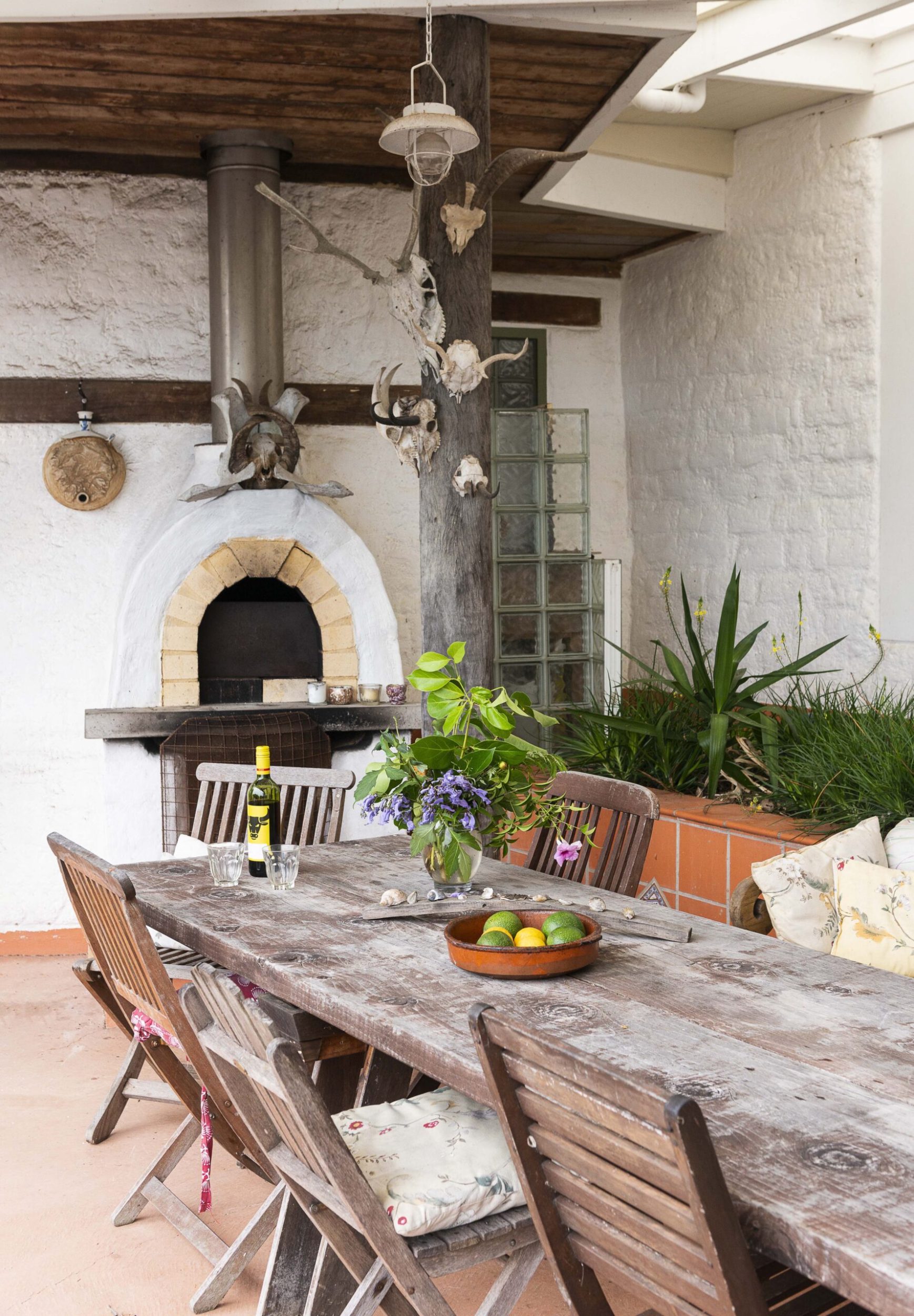 An outdoor living area with a pizza oven, a rustic brown table and greenery