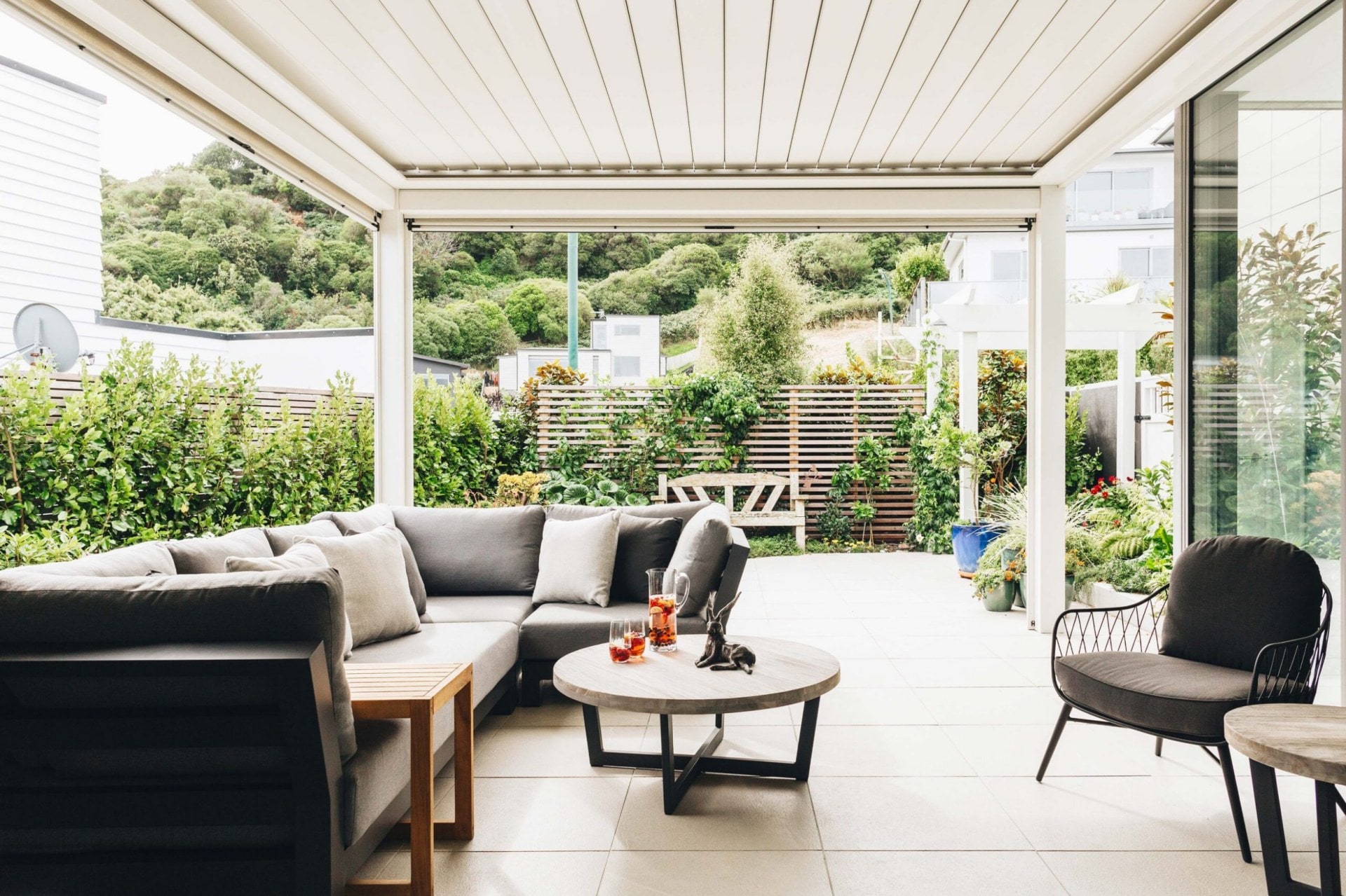 An outdoor area with grey tiles, grey seats and large glass windows